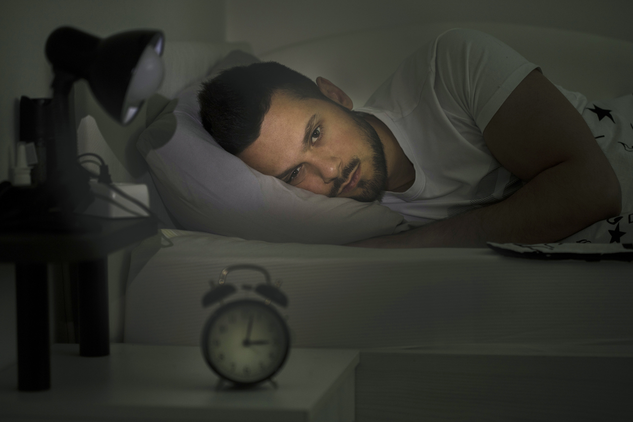 Young man awake at night with clock pointing to 3am